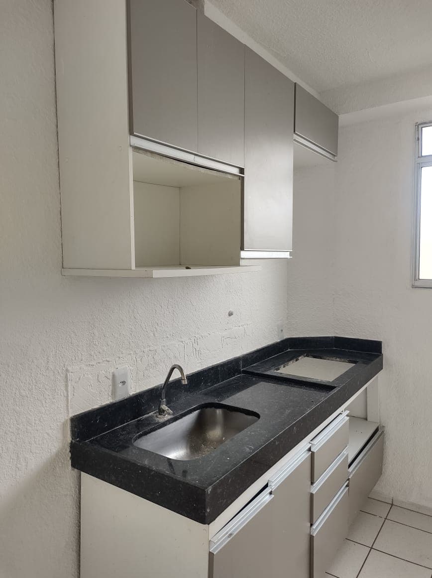 Cozinha com bancada de granito preto, pia de inox e armários planejados em tom cinza.