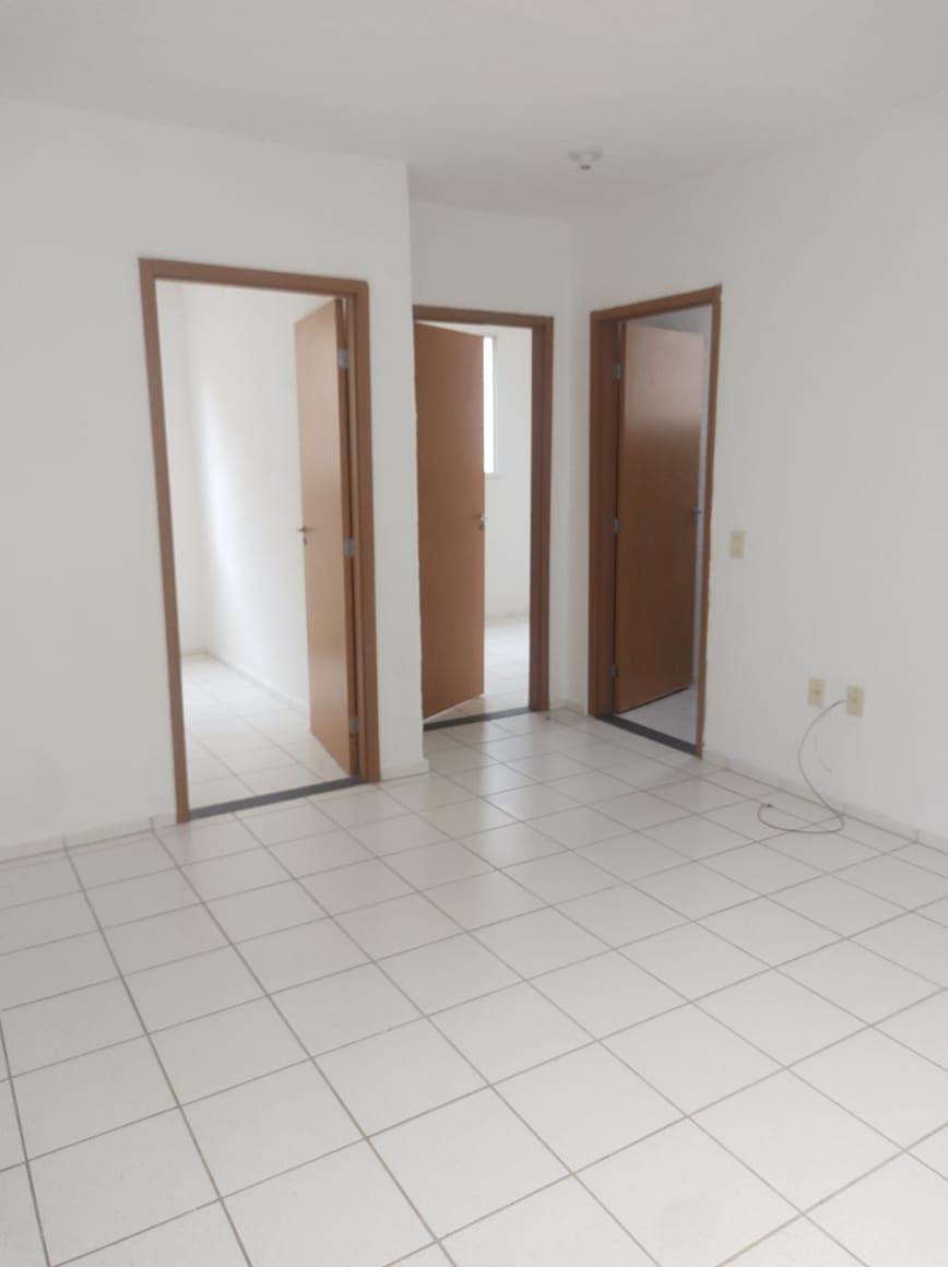 Sala de estar com piso de cerâmica clara, paredes brancas e três portas de madeira que dão acesso a outros cômodos.
