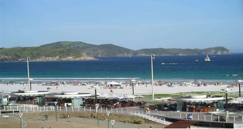 Vista panorâmica da praia com mar azul, faixa de areia e quiosques próximos.