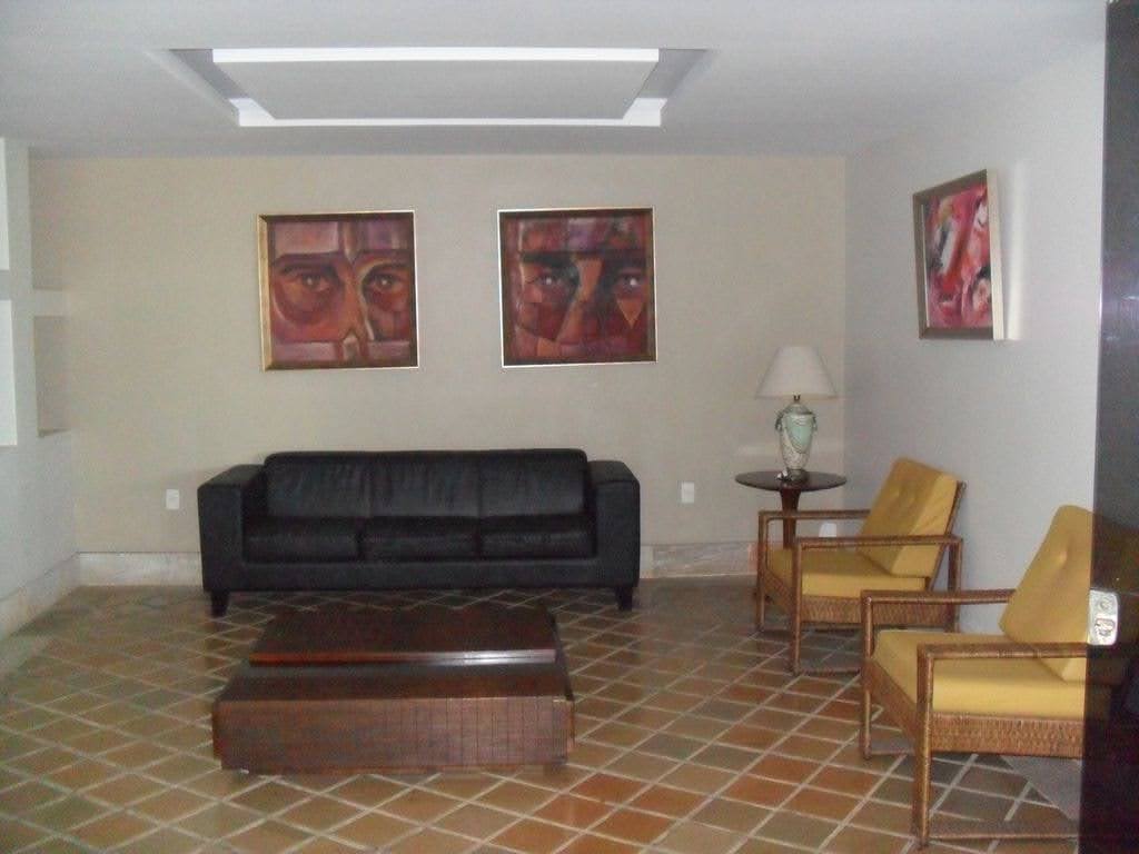 Sala de espera ou recepção com sofá preto, poltronas amarelas e quadros nas paredes.